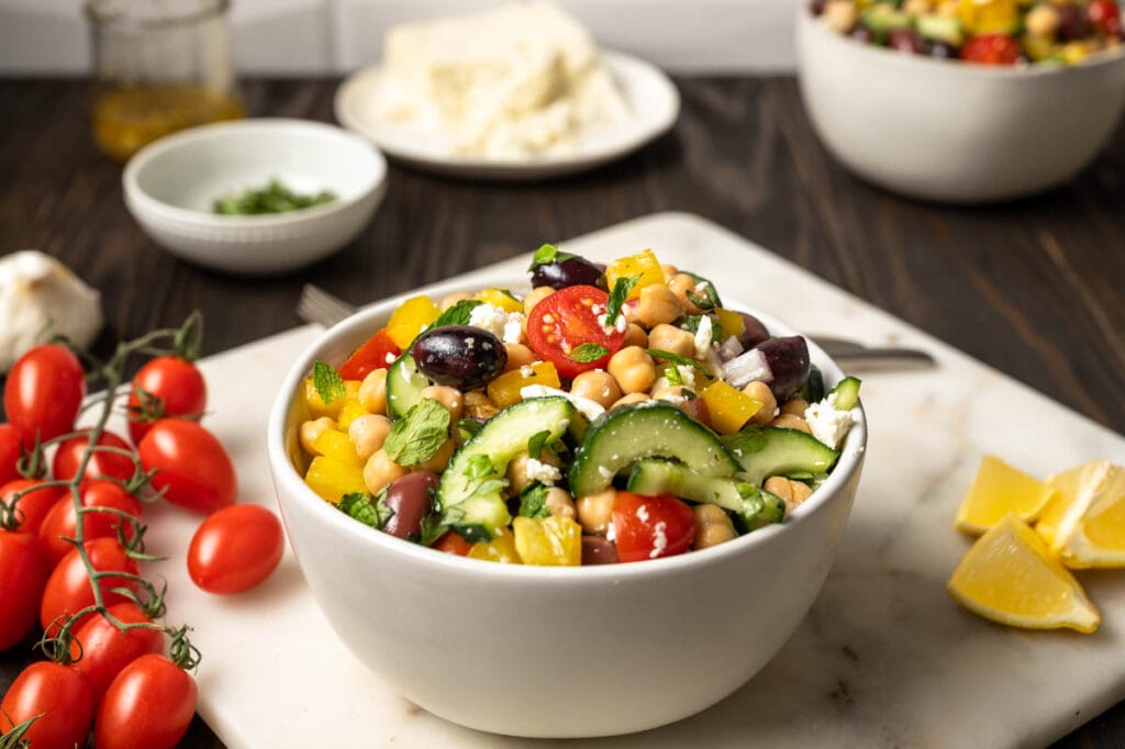 Bowl of chickpea salad with feta, olives bright red cherry tomatoes and cucumber.