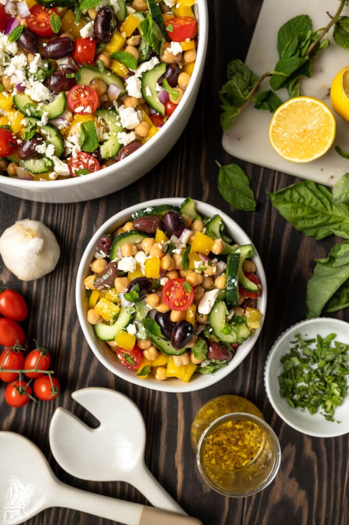 Bowl of chickpea salad with feta, olives bright red cherry tomatoes and cucumber.