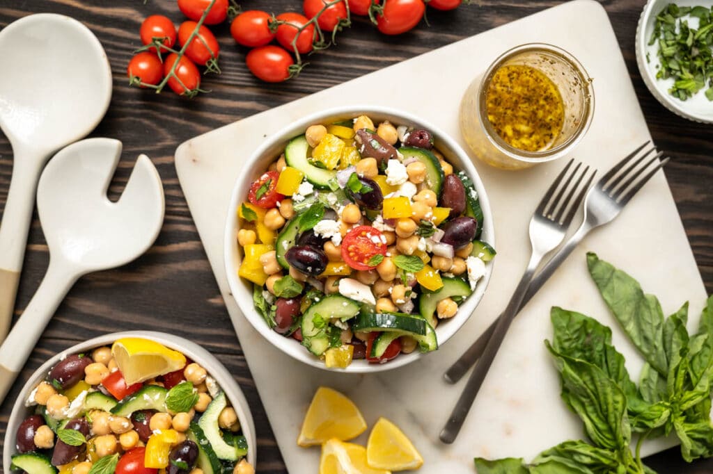 Bowl of chickpea salad with feta, olives bright red cherry tomatoes and cucumber.