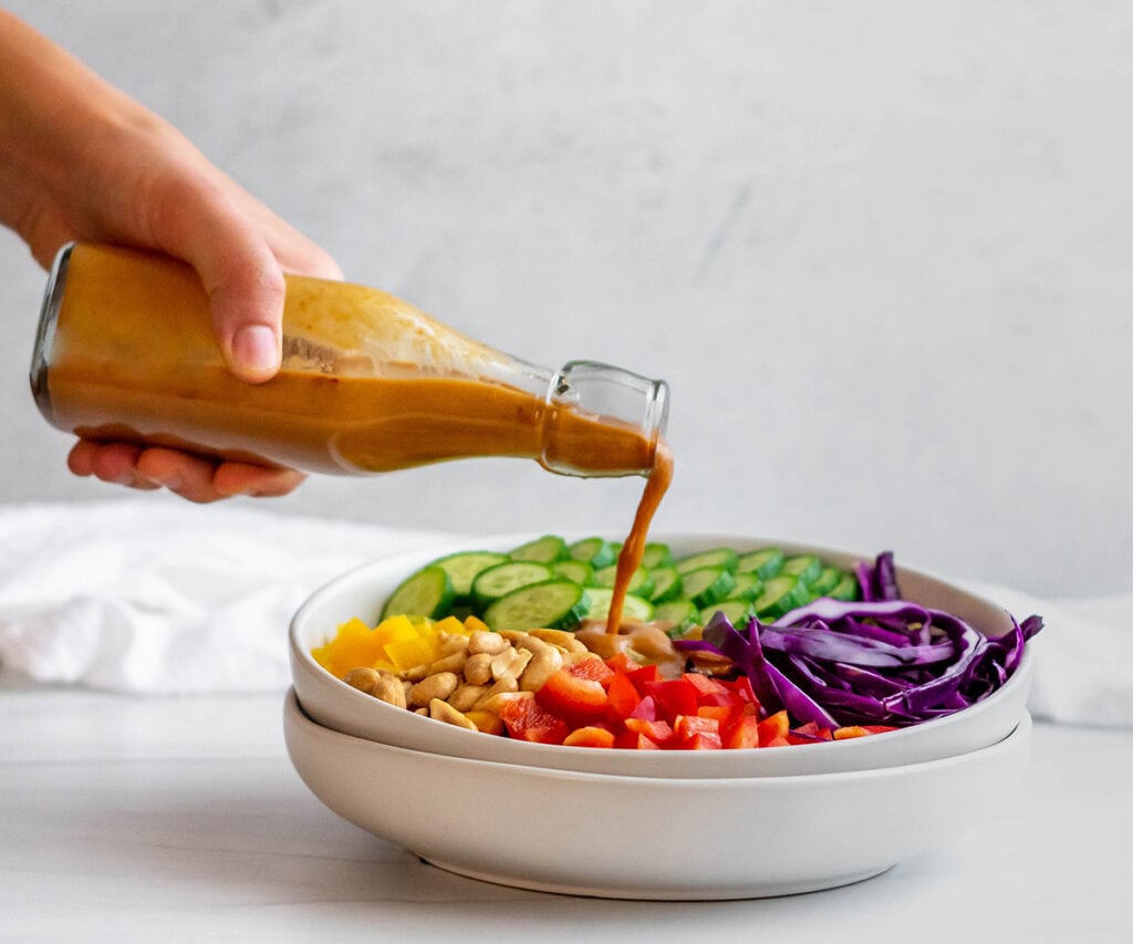 Thai peanut dressing being poured on to a salad.