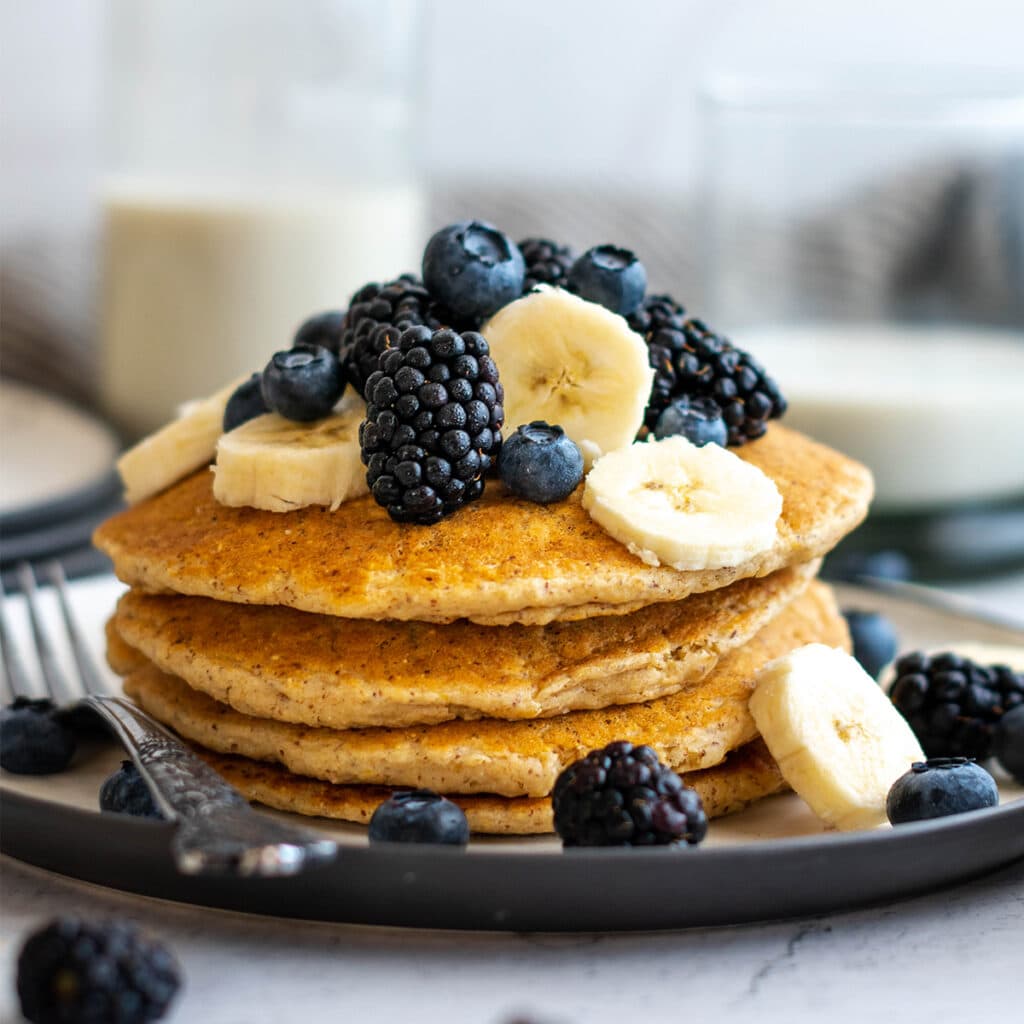 Stack of vegan oatmeal pancakes with blackberries, blueberries and banana on top.