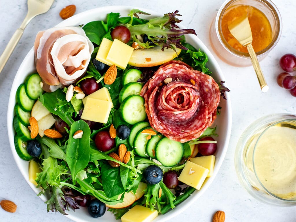 Charcuterie salad with nuts, salami, cheese, grapes, blueberries, olives and cucumbers.