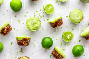 Bright green mini paleo vegan key lime tarts and limes laying on white tile counter.