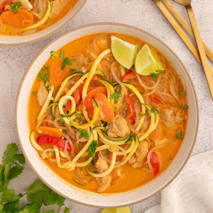 Red curry chicken soup garnished with limes and cilantro in a bowl.