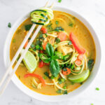 Paleo and Keto Thai Curry Chicken Zoodle Soup with basil, Thai chilis, bell pepper, lime, carrots, and chicken thighs.