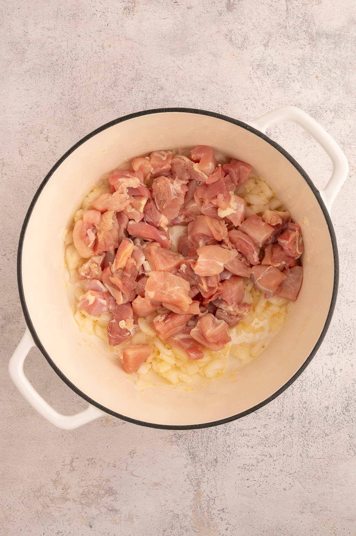 Diced chicken thighs added to stock pot with onions.