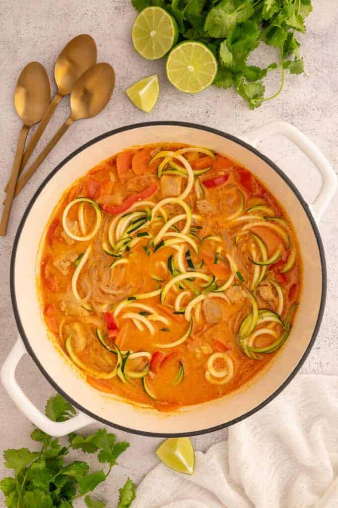 Finished red curry chicken soup with sweet potato glass noodles and zucchini noodles in a large white stock pot.