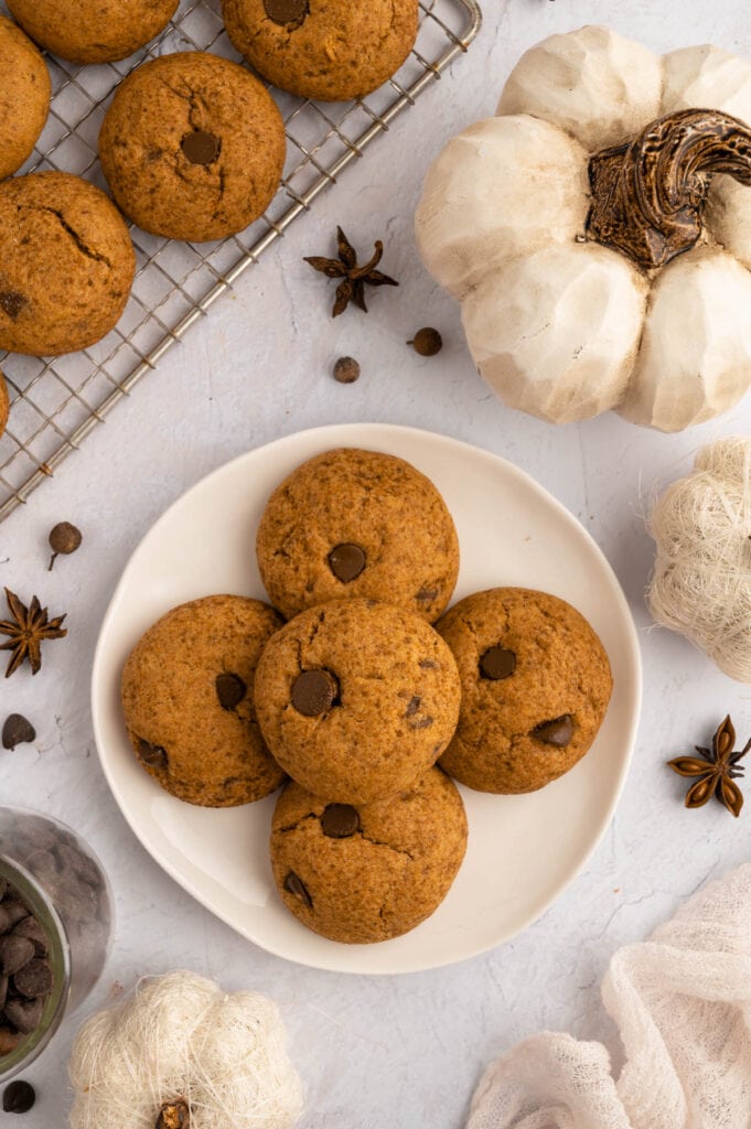 Wire rack of gluten free pumpkin chocolate chip cookies next to a wire rack full of cookies and cinnamon sticks..