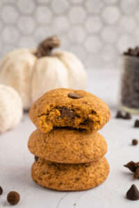Stack of pumpkin chocolate chip cookies with white pumpkins in the background.