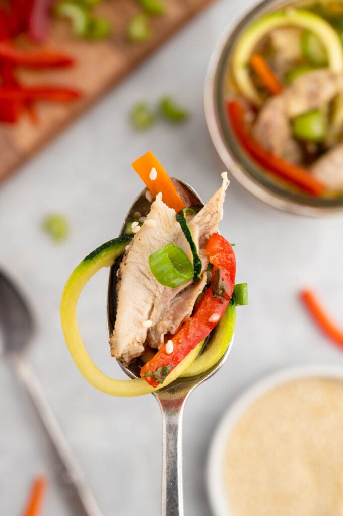 Spoon with broth, thinly sliced chicken thigh and colorful veggies.