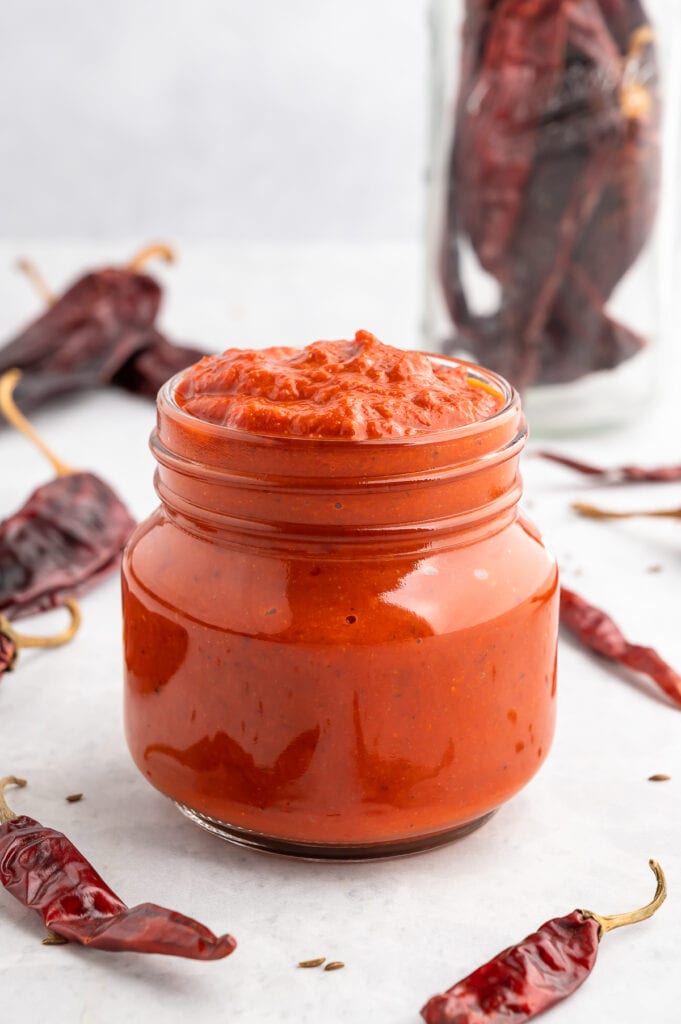 Jar of harissa sauce next to peppers.