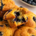 Gluten-free blueberry muffins piled on a plate, one with a bite out of it.