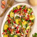 Platter with large salad with strawberries, goat cheese, walnuts, avocado and pickled onions.