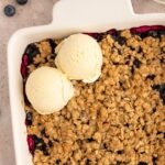 Gluten-free blueberry crisp with ice cream scoops on top.