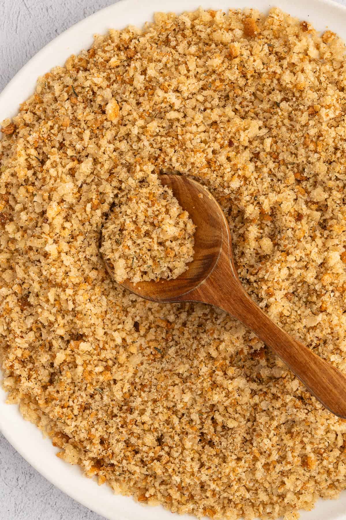 Gluten-free bread crumbs in bowl with wooden spoon.