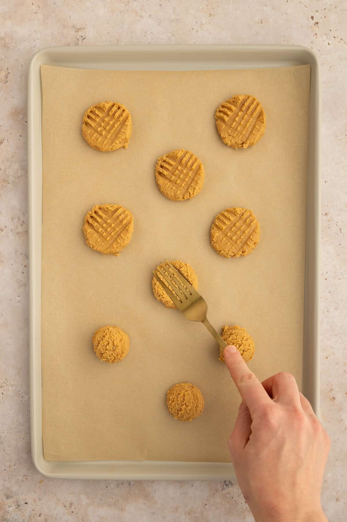 Pressing the cookie dough using a fork to create a cross hatch design.
