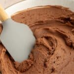 Bowl of chocolate buttercream frosting with a spatula in it.