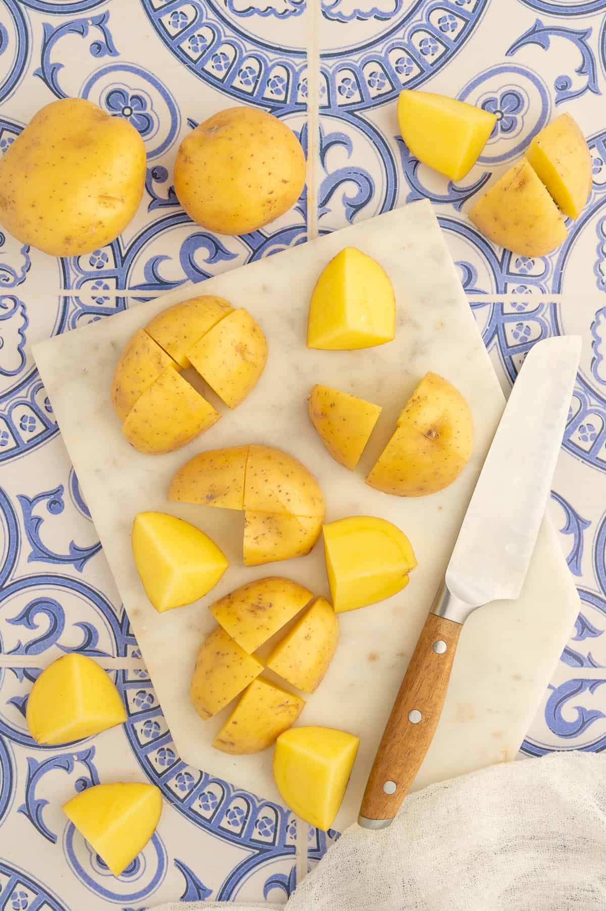 Halving yellow potatoes on a cutting board and then cutting into quarters.
