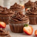 Gluten-free chocolate cupcakes topped with a swirl of chocolate buttercream frosting next to strawberries.