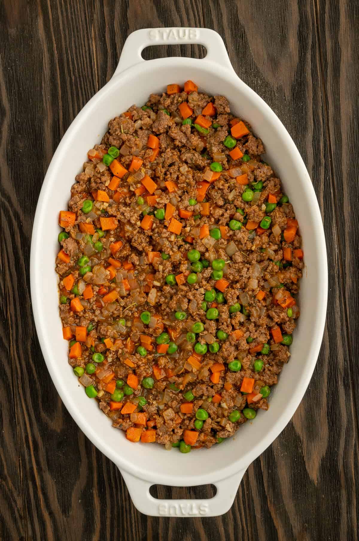 Transferring meat mixture to white oval casserole dish.