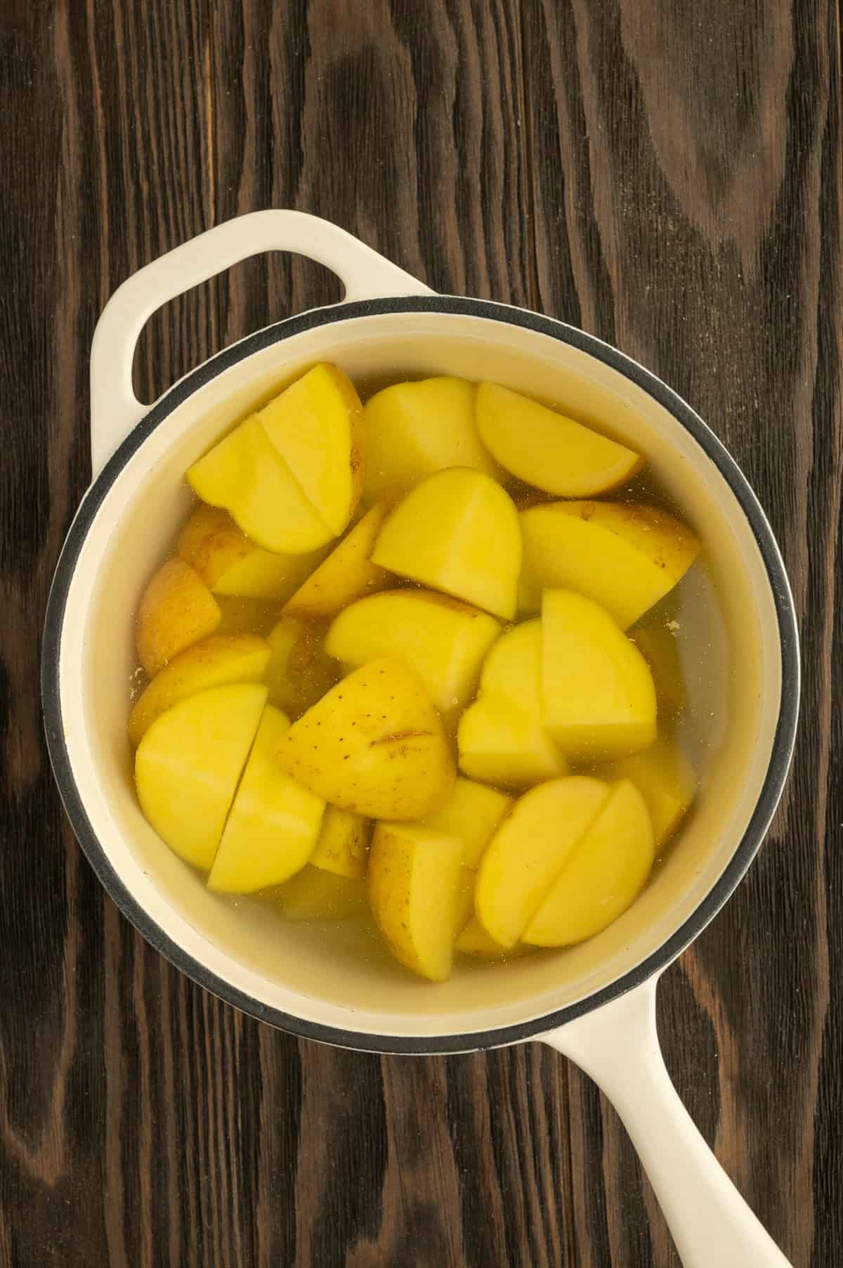 Potatoes quartered and boiling in a pot.