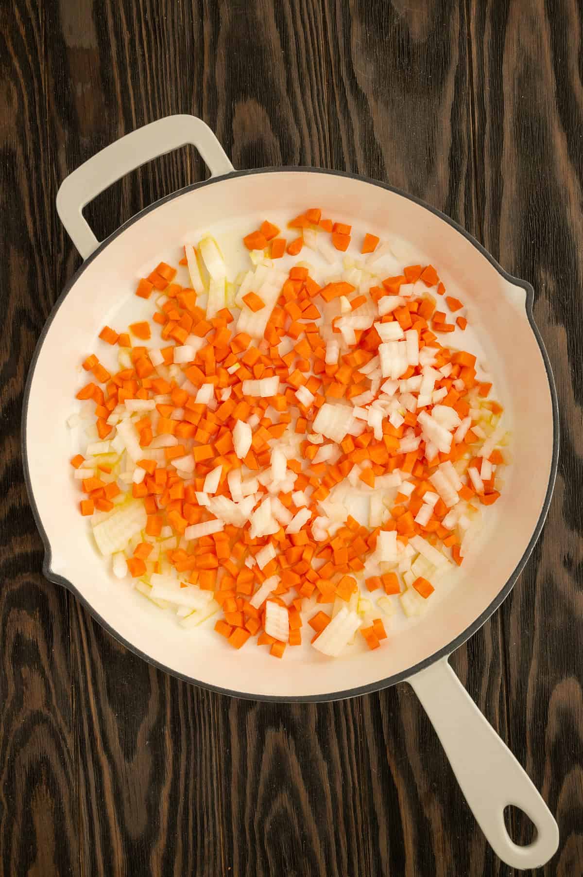 Sautéing carrots, onions and garlic in a white skillet.