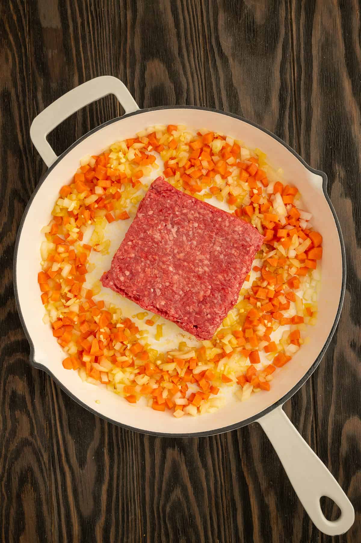 Adding ground beef to skillet with carrots, onions and garlic.