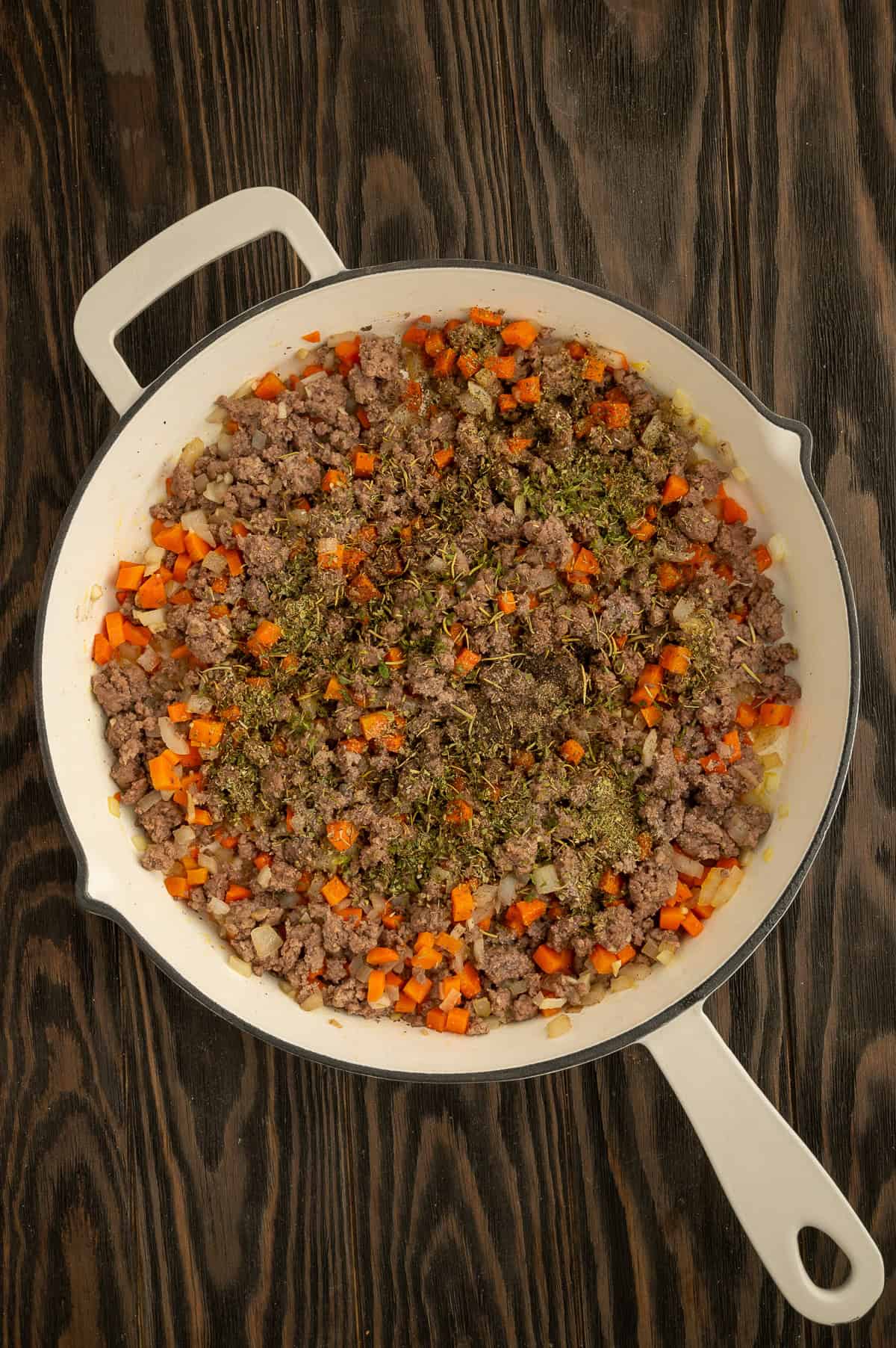 Adding seasonings to the skillet with the beef and veggies.
