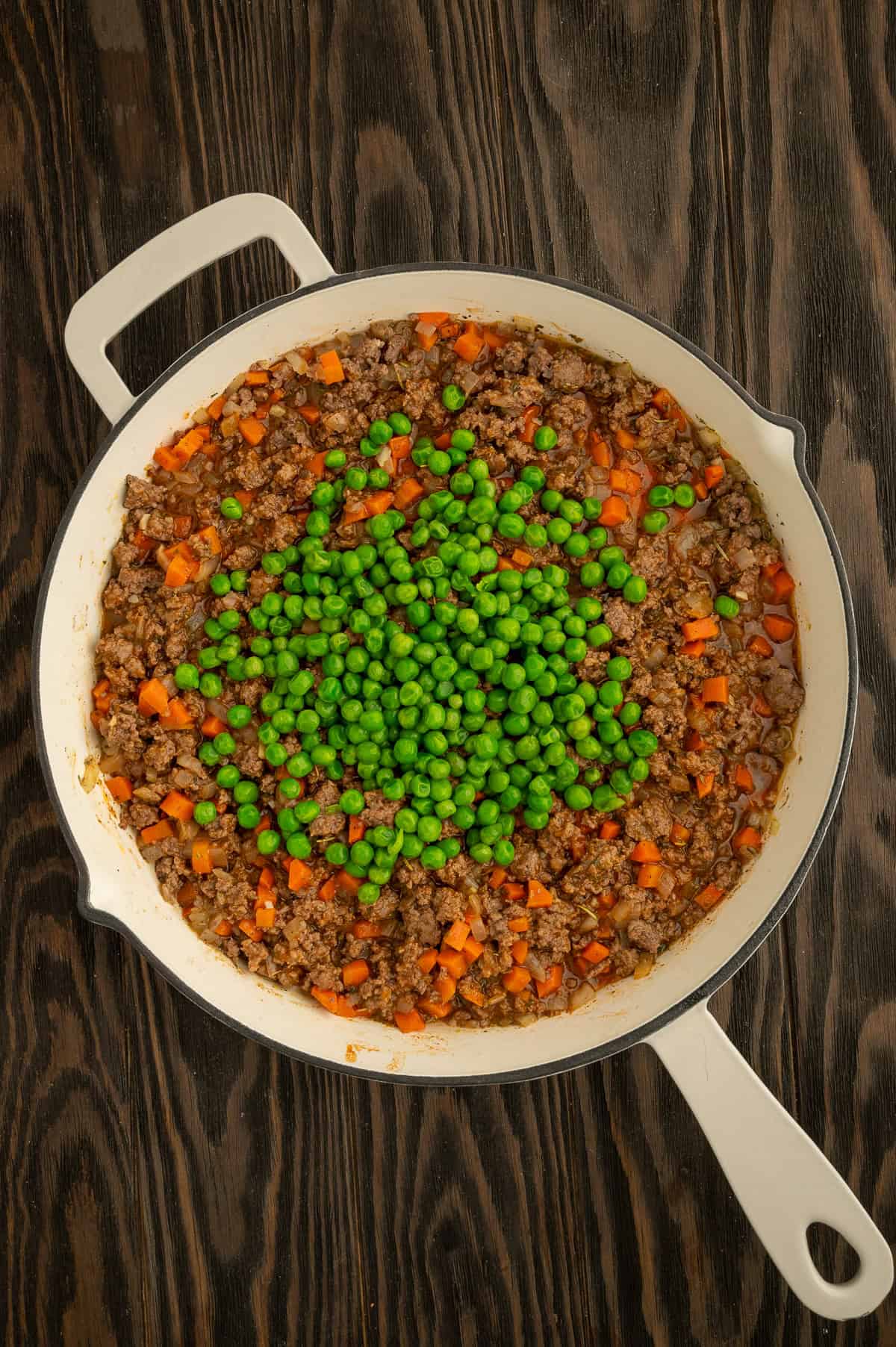 Adding peas to skillet with sauce and meat.