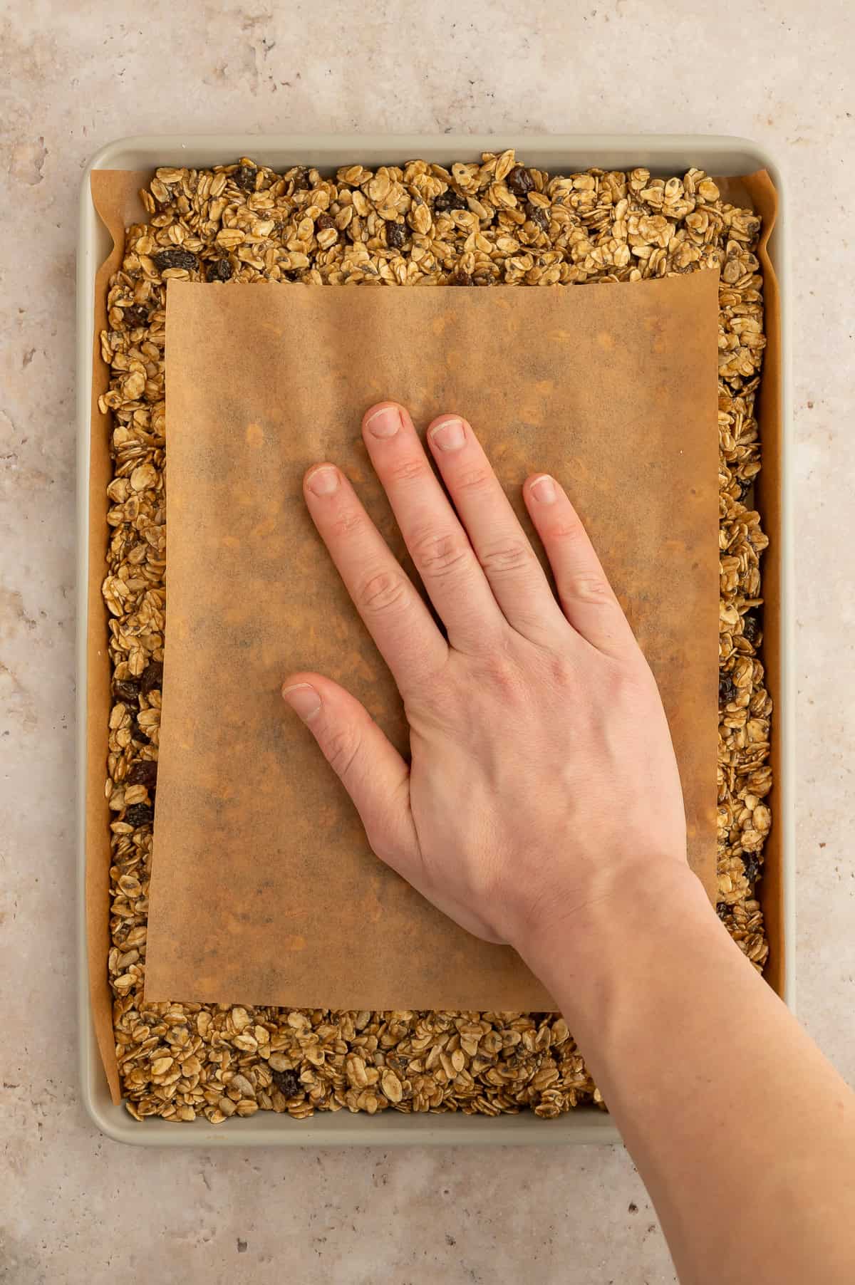 Hand using a piece of parchment paper to pack the granola.