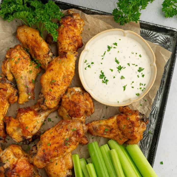 Platter of crispy gluten-free chicken wings next to celery, parsley, and cottage cheese ranch dressing.