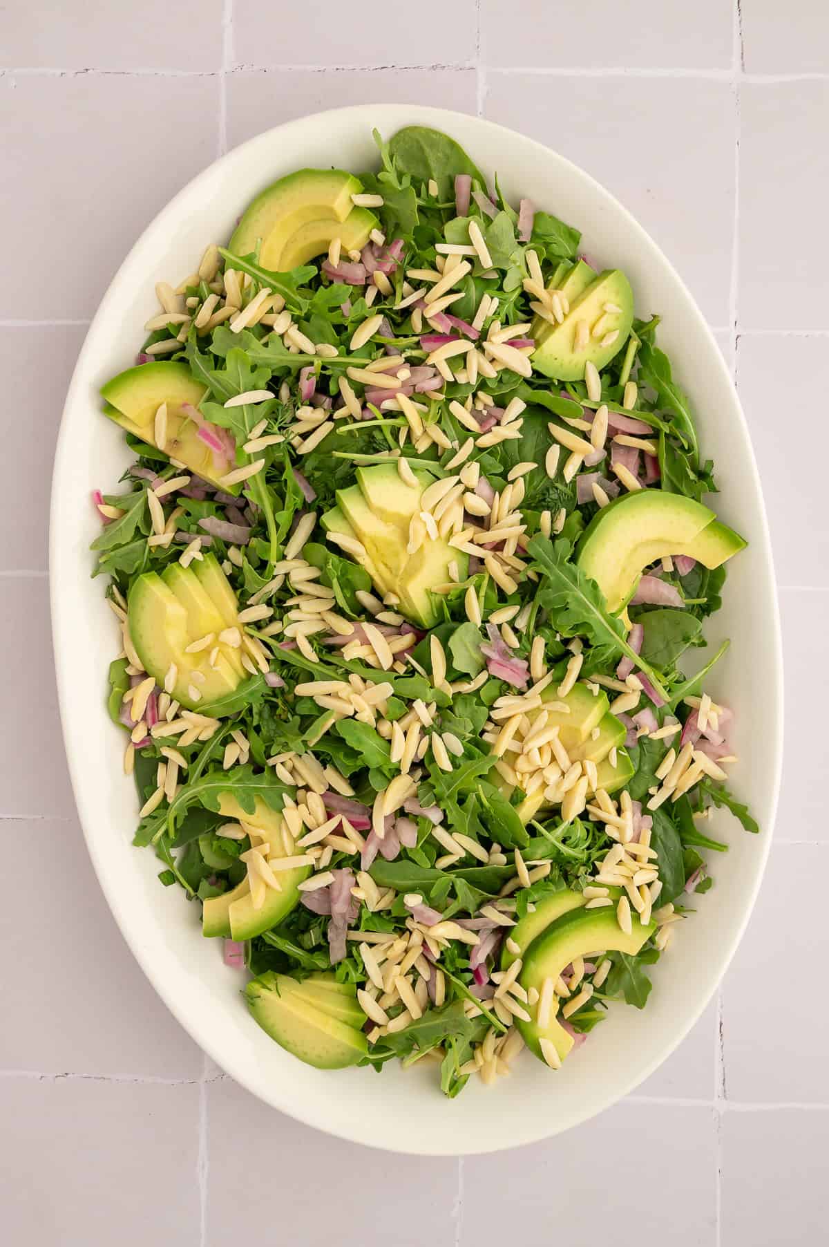 Arugula, spinach, pickled onion, dill, mint, avocado, and slivered almonds on white platter.