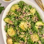 Salad on a white platter with arugula, spinach, slivered almonds, dill, mint, and avocado.