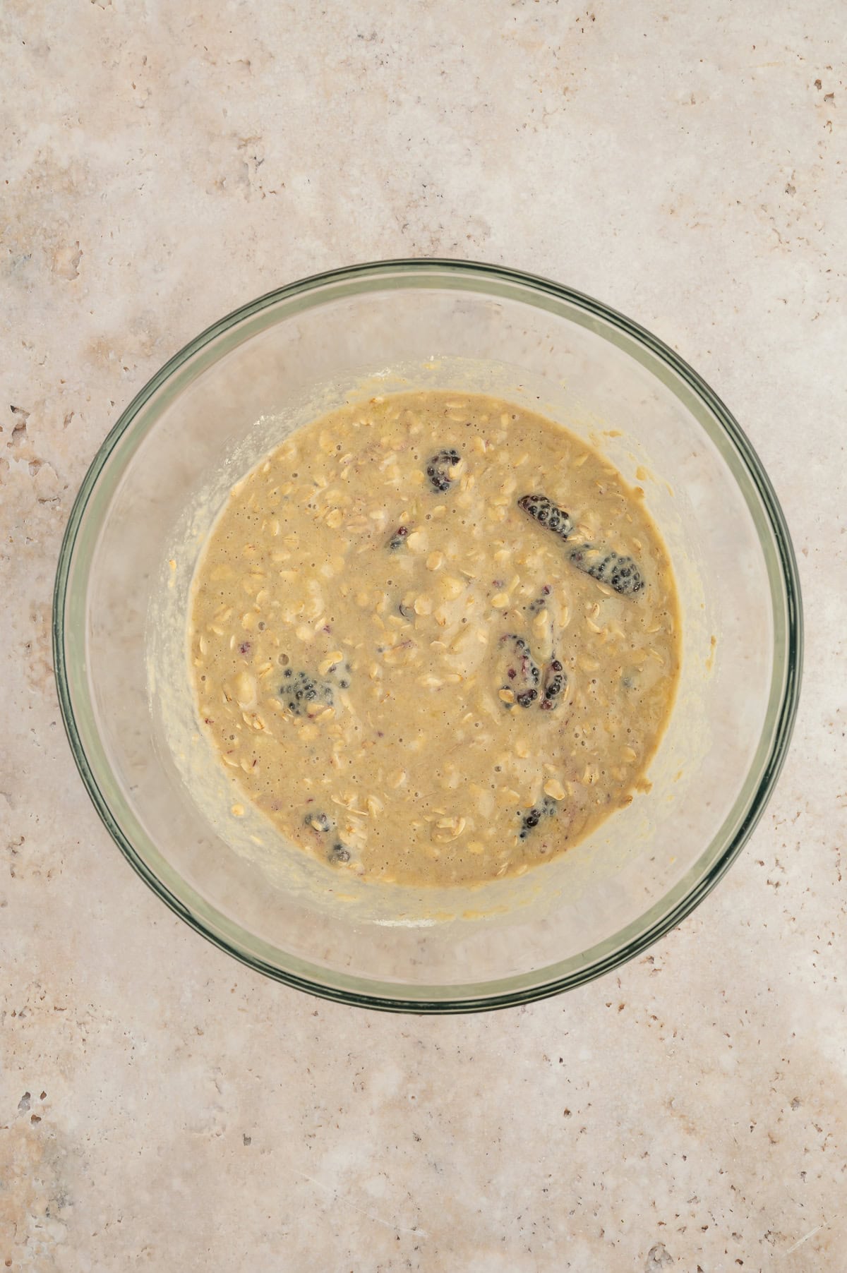 Mixing together all ingredients for banana blackberry oatmeal muffins and folding in blackberries into a mixing bowl.