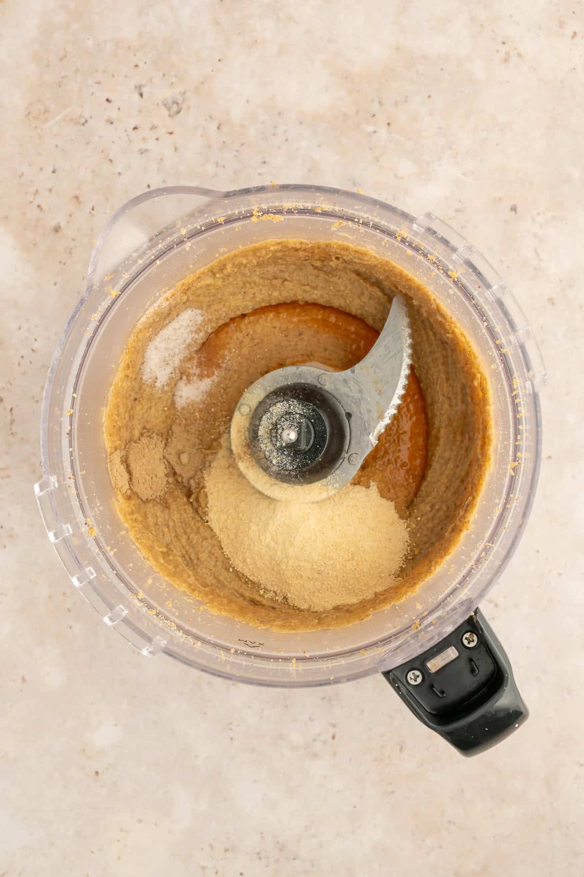 Food processor with smooth walnut butter with maple sugar, sea salt, vanilla, and cardamon in it.