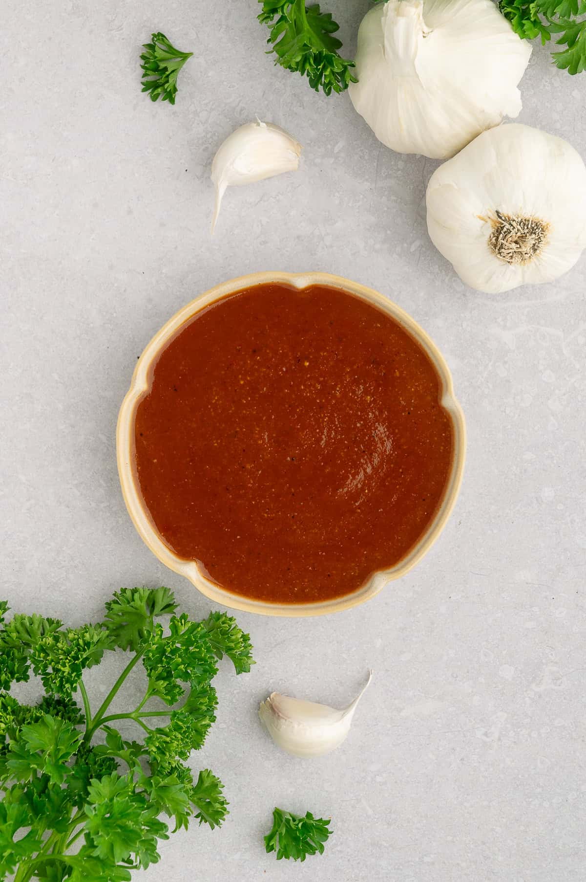 Dish of BBQ sauce next to garlic and parsley.