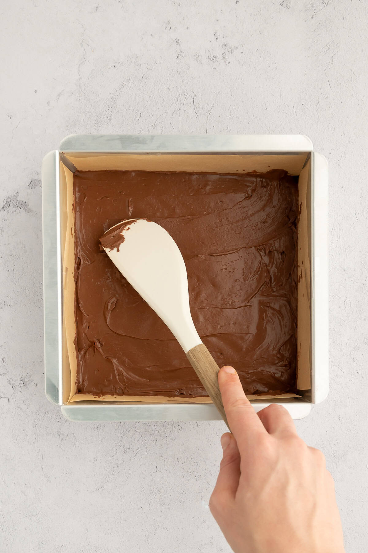 Transferring fudge to a lined baking pan.