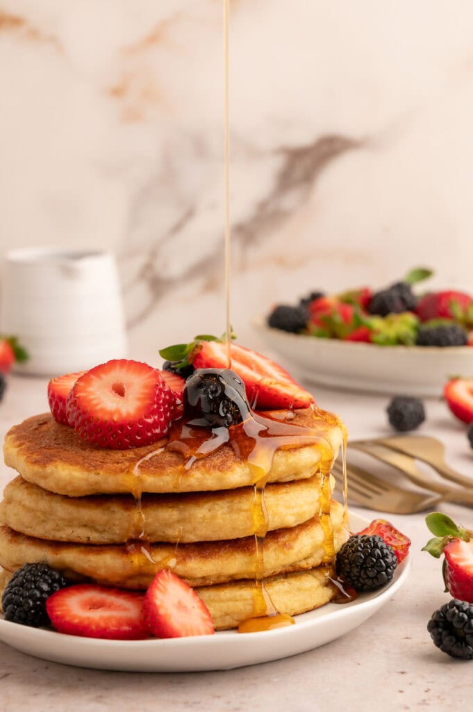 Stack of protein pancakes topped with berries and syrup being poured on top.