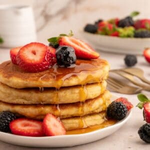 Stack of protein pancakes with dripping syrup and berries.