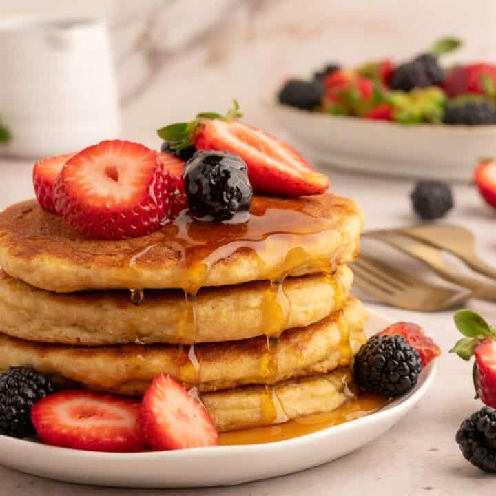 Stack of protein pancakes with dripping syrup and berries.