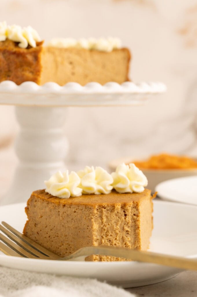 Slice of protein pumpkin cheesecake with whipped cream on top and a forked off piece.