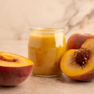 Peach salad dressing in a jar next to halved peaches.