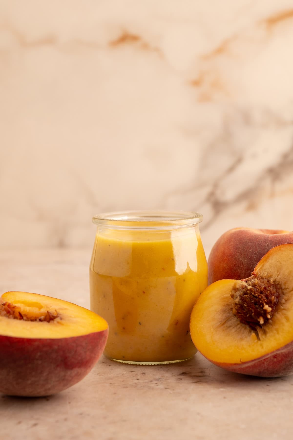 Peach salad dressing in a jar next to halved peaches.