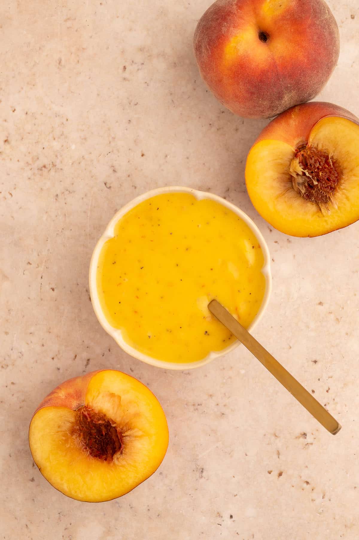 Peach salad dressing in a flower shaped bowl, next to halved peaches.