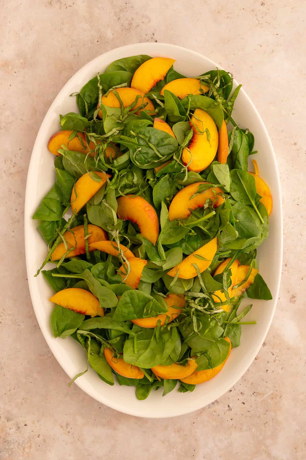 Sliced peaches and shredded basil added to platter with spinach.