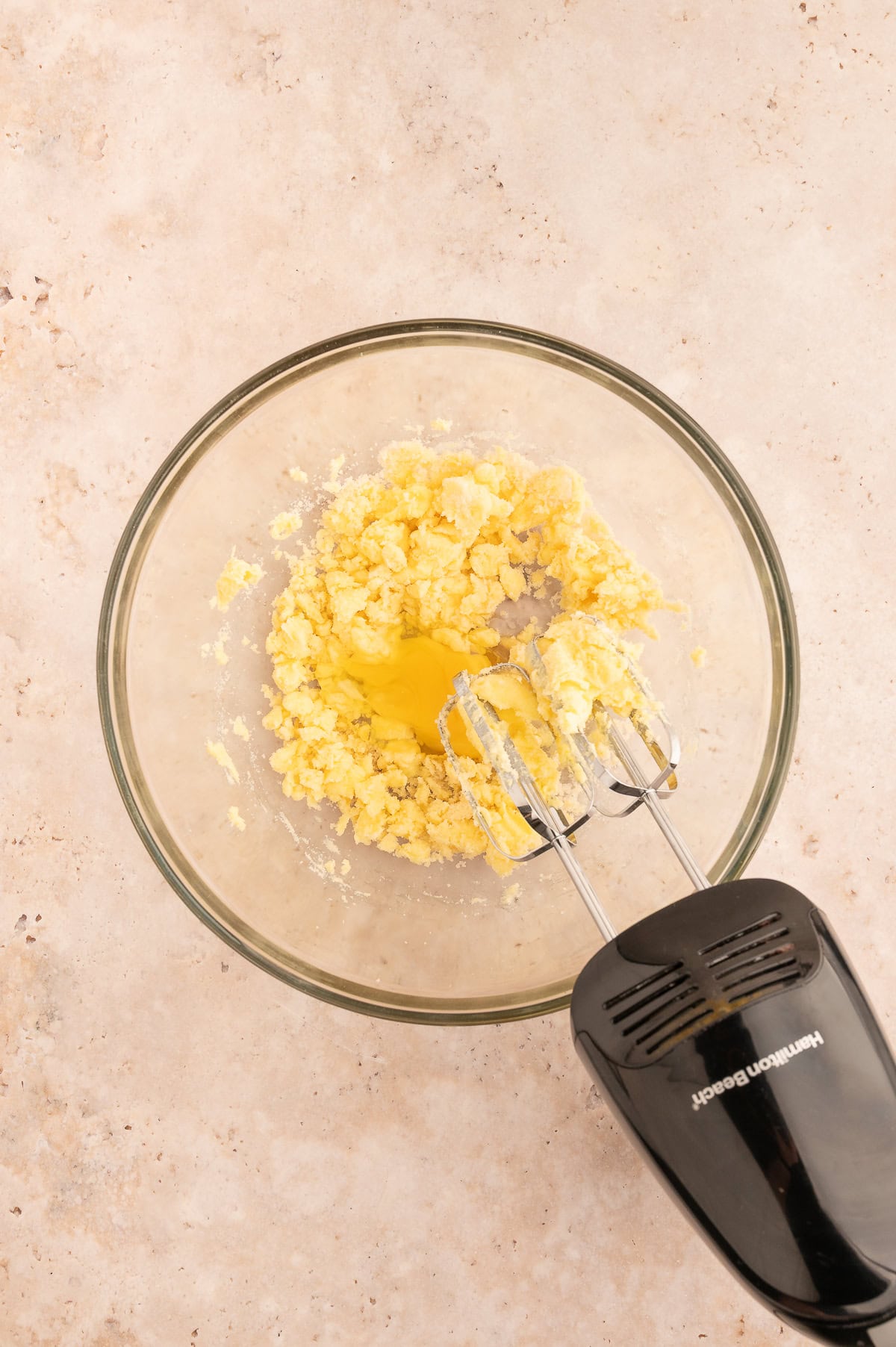 Electric handheld mixer in a bowl with creamed butter and sugar, adding the egg.