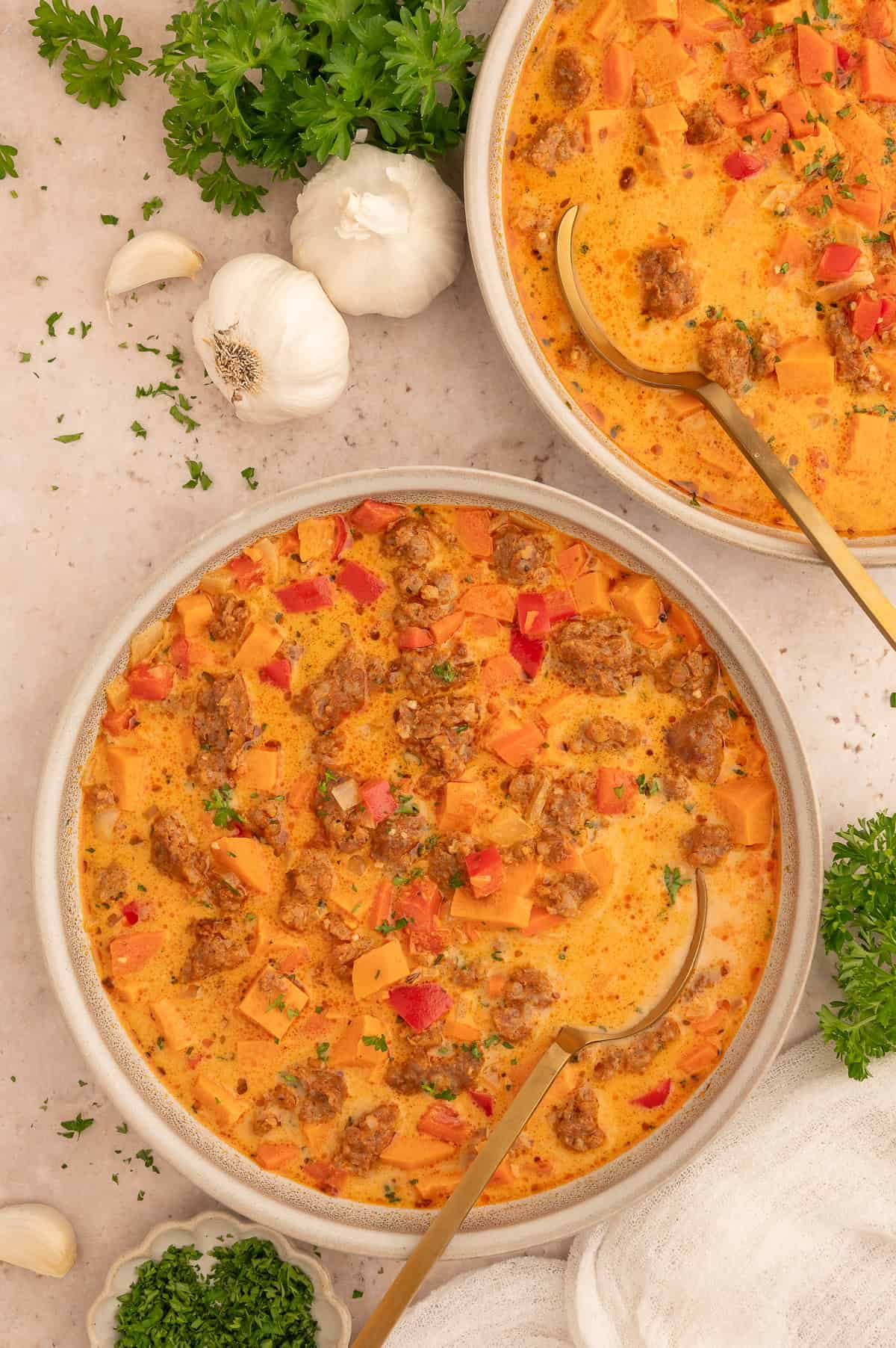 Bowl of sweet potato and chorizo soup with a spoon in it.