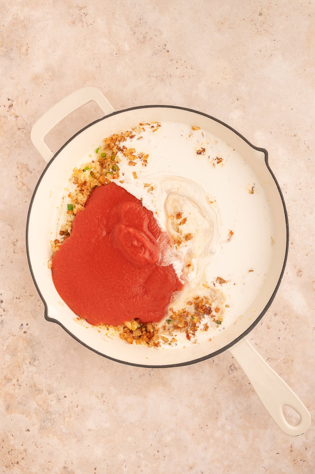 Adding coconut milk and tomato sauce to the skillet.