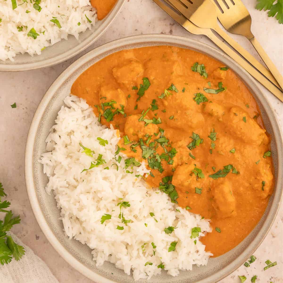 Richly orange colored dairy-free tikka masala in a bowl with rice and topped with cilantro.