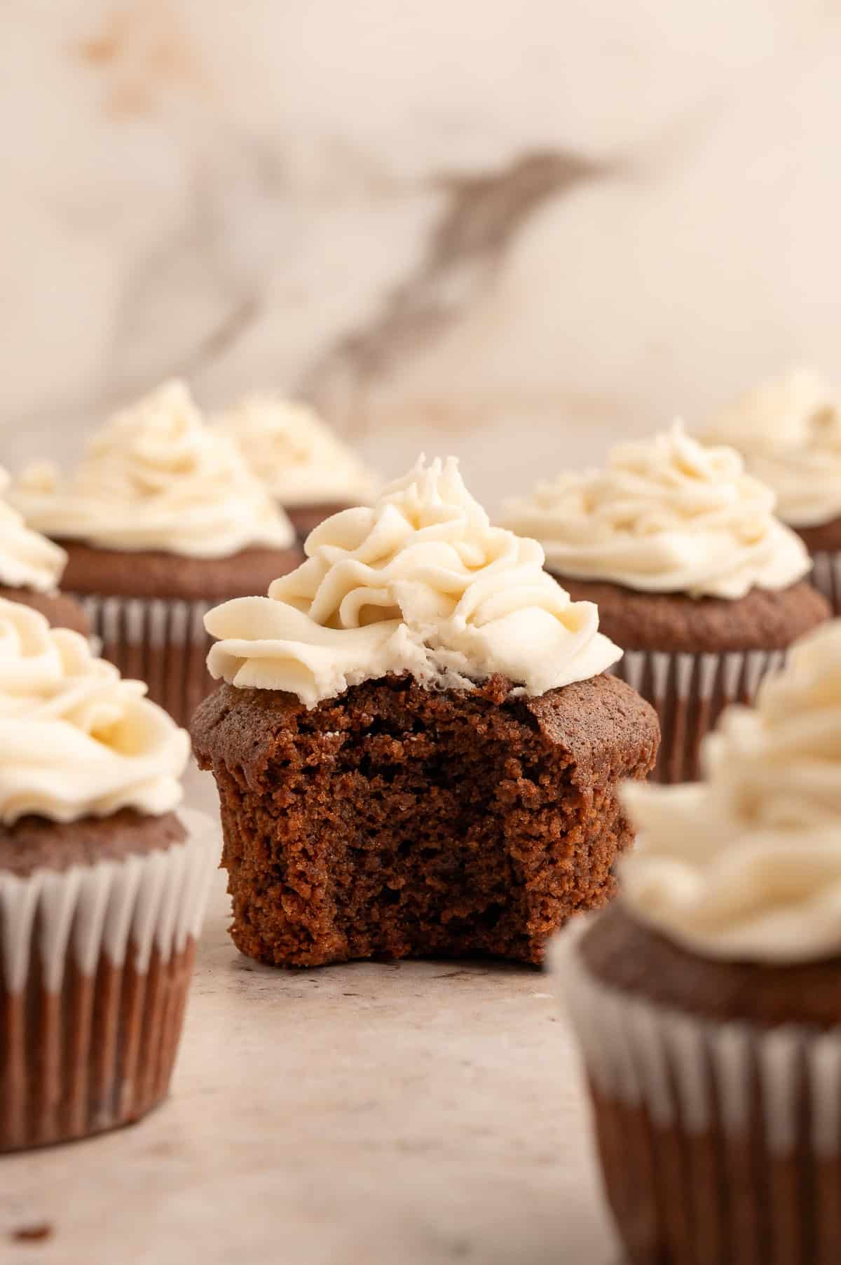 An almond flour chocolate cupcake with white frosting and a bite out of it showing the moist center.